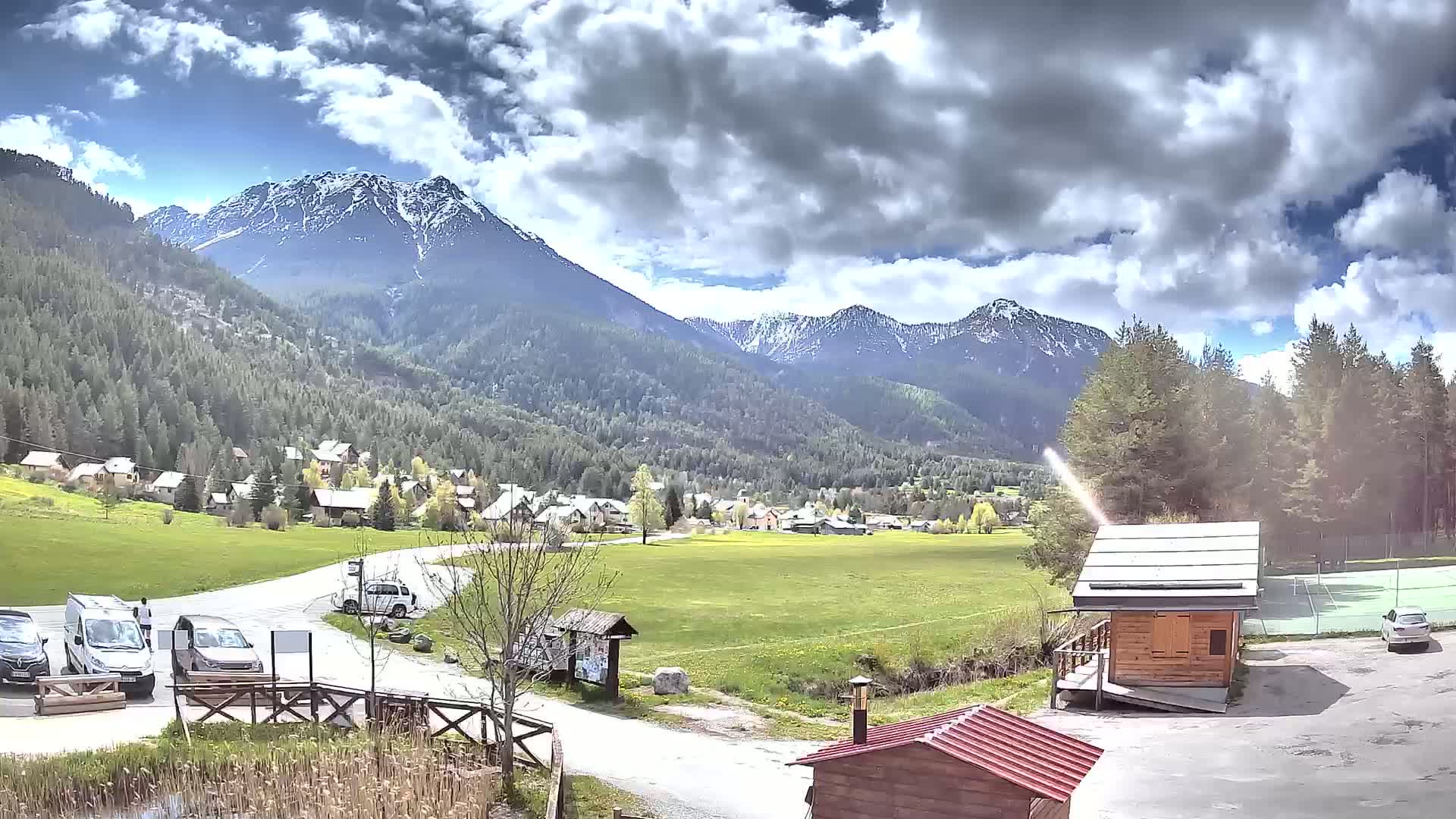 A partly cloudy day reveals a mountain valley town nestled amongst snow-capped mountains and evergreen forests.