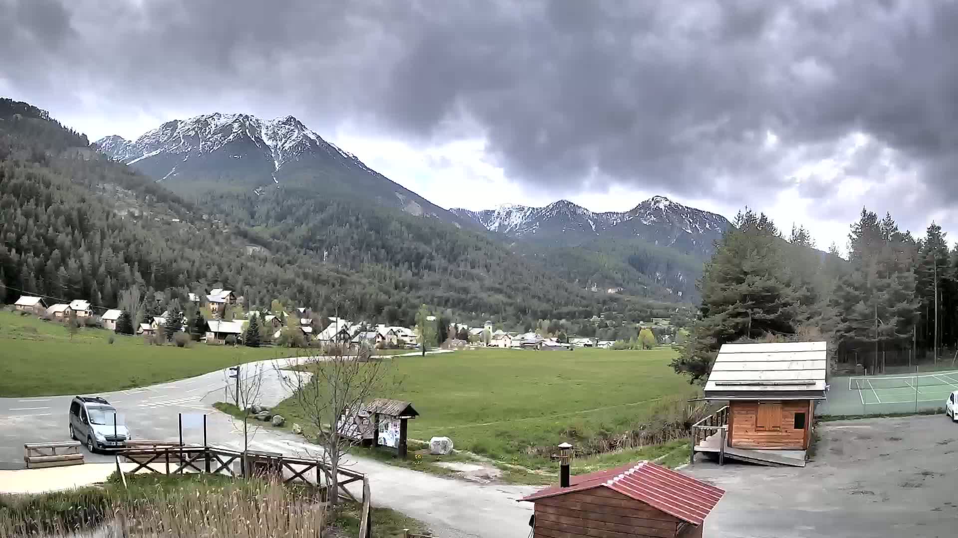 A small village nestled in a valley between snow-capped mountains under a cloudy sky.