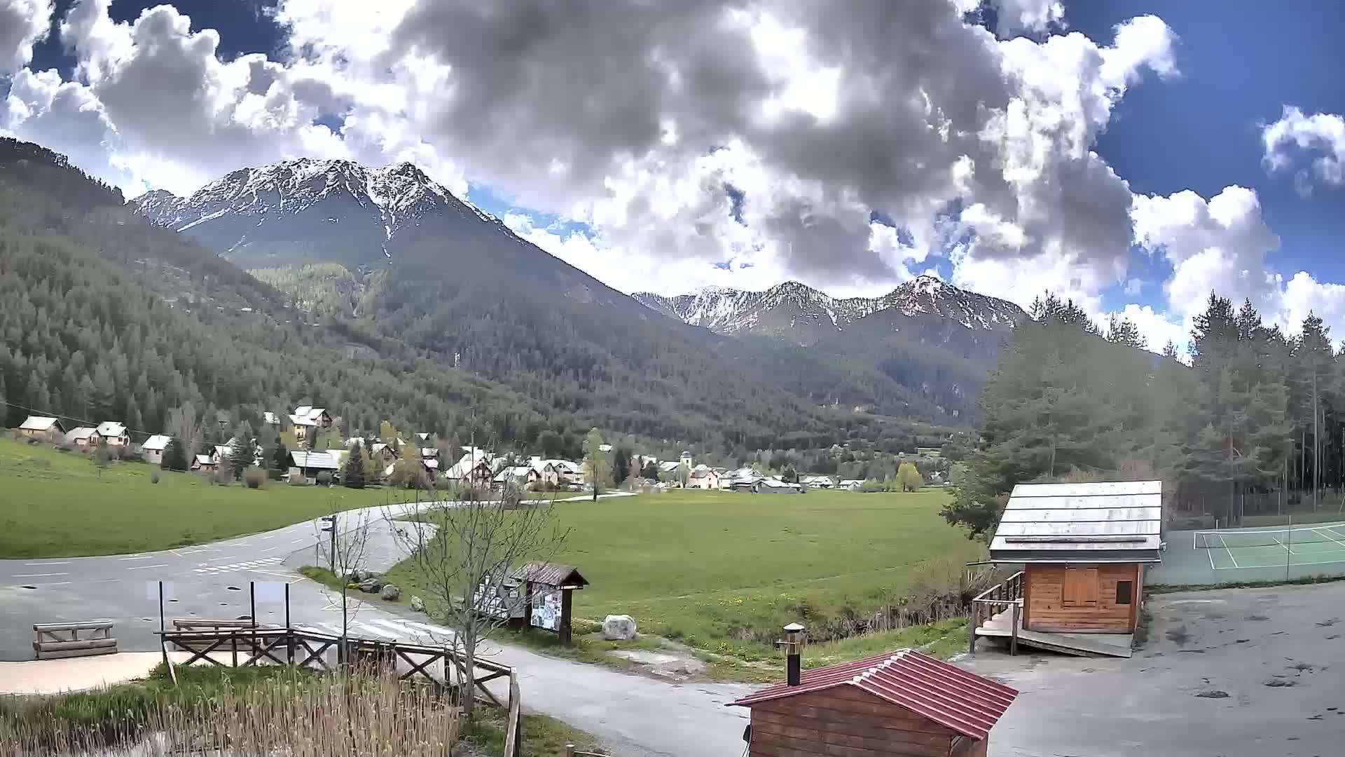 A small village nestled in a valley between snow-capped mountains under a partly cloudy sky.
