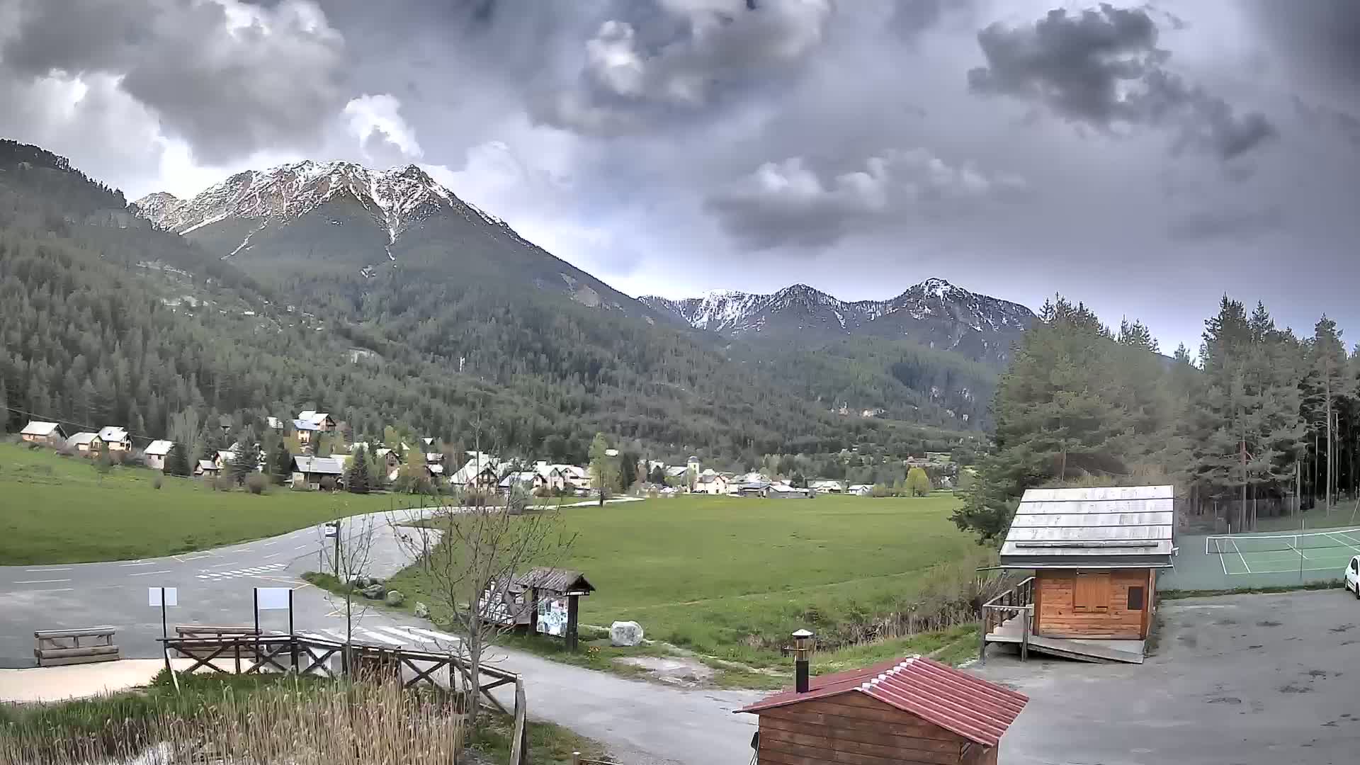 A small village nestled in a valley between snow-capped mountains under a cloudy sky.
