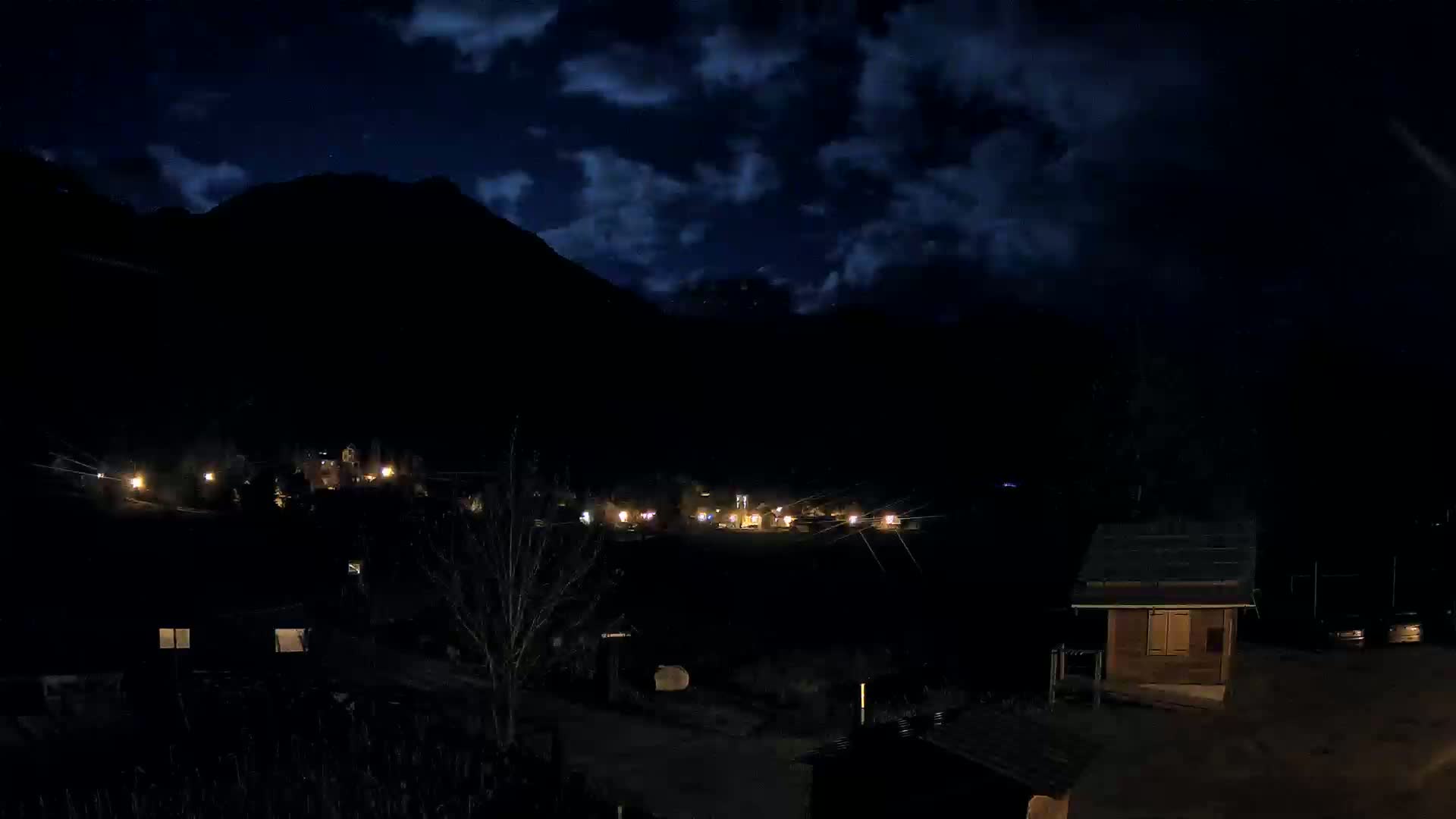 A small village nestled in a dark mountain valley at night under a partly cloudy sky.