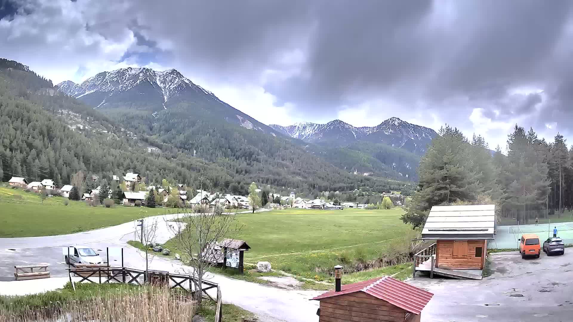 A small village nestled in a valley between snow-capped mountains under a cloudy sky.