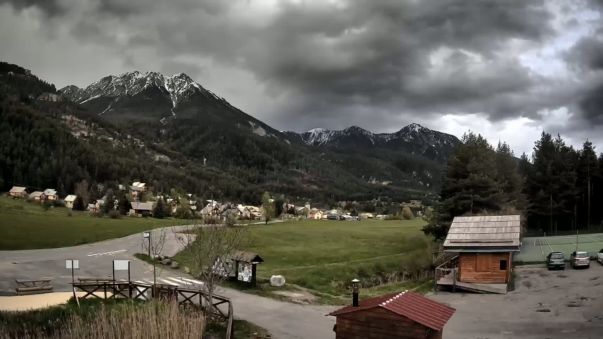 A small village nestled in a valley between snow-capped mountains under a cloudy sky.