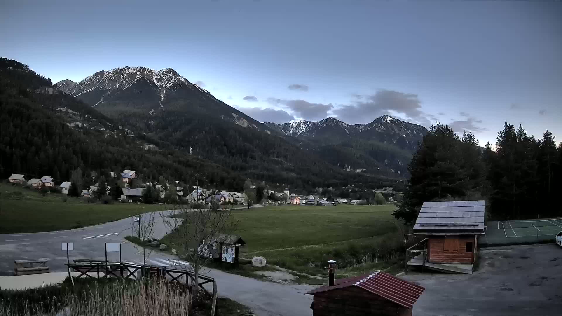 A small village nestled in a valley between snow-capped mountains under a twilight sky.