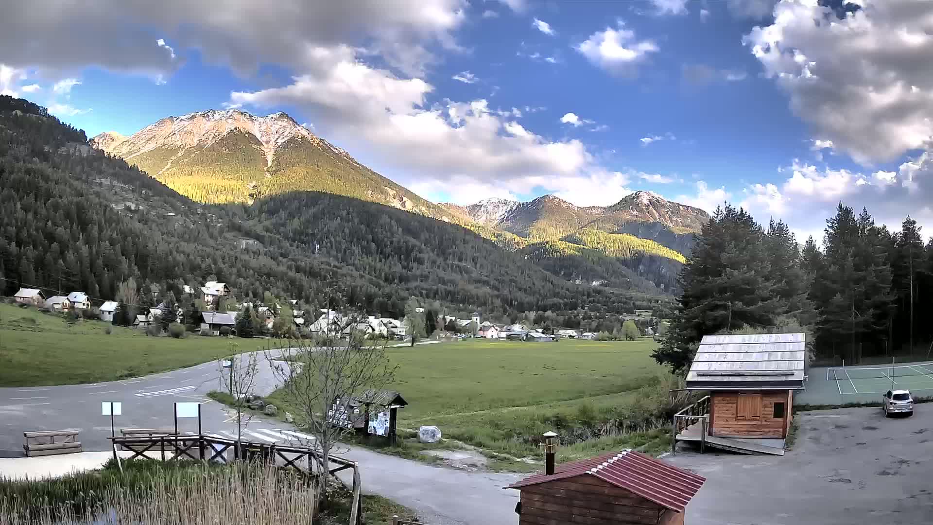 A small village nestled in a valley between mountains under a partly cloudy sky.
