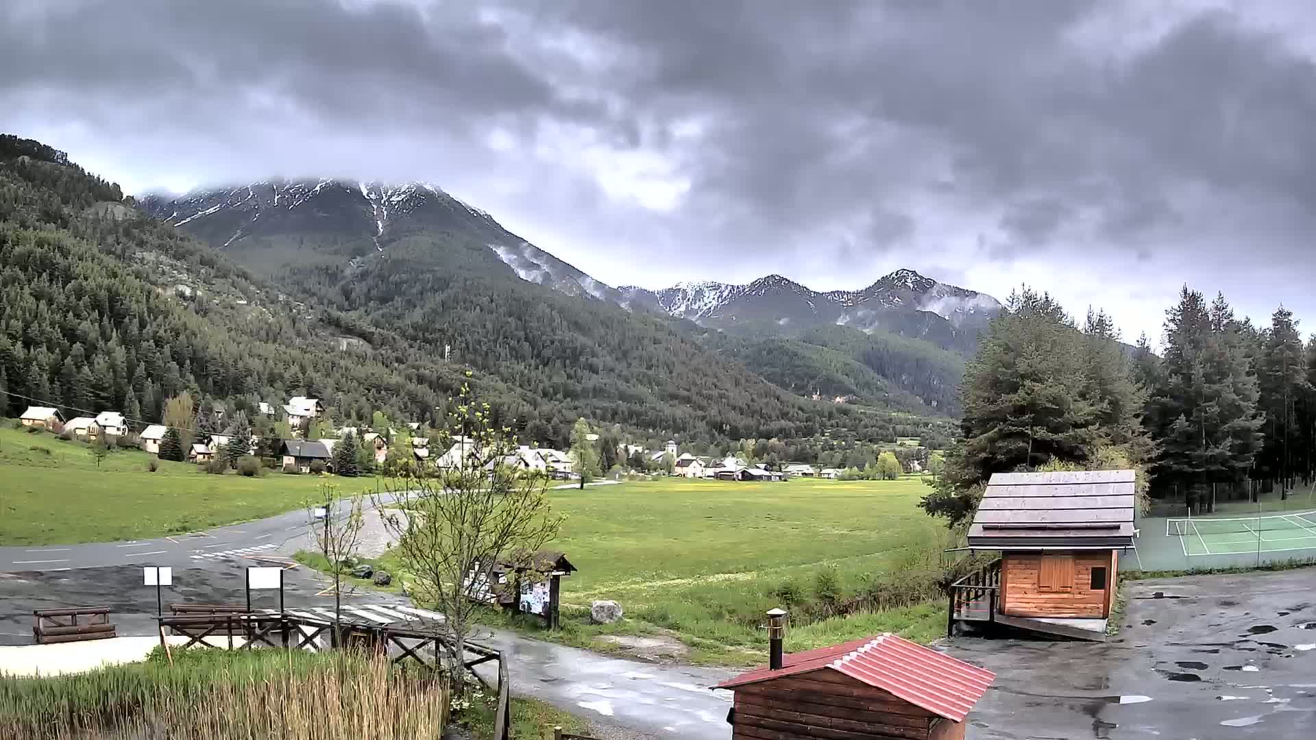 A small village nestled in a valley between snow-capped mountains under a cloudy sky.