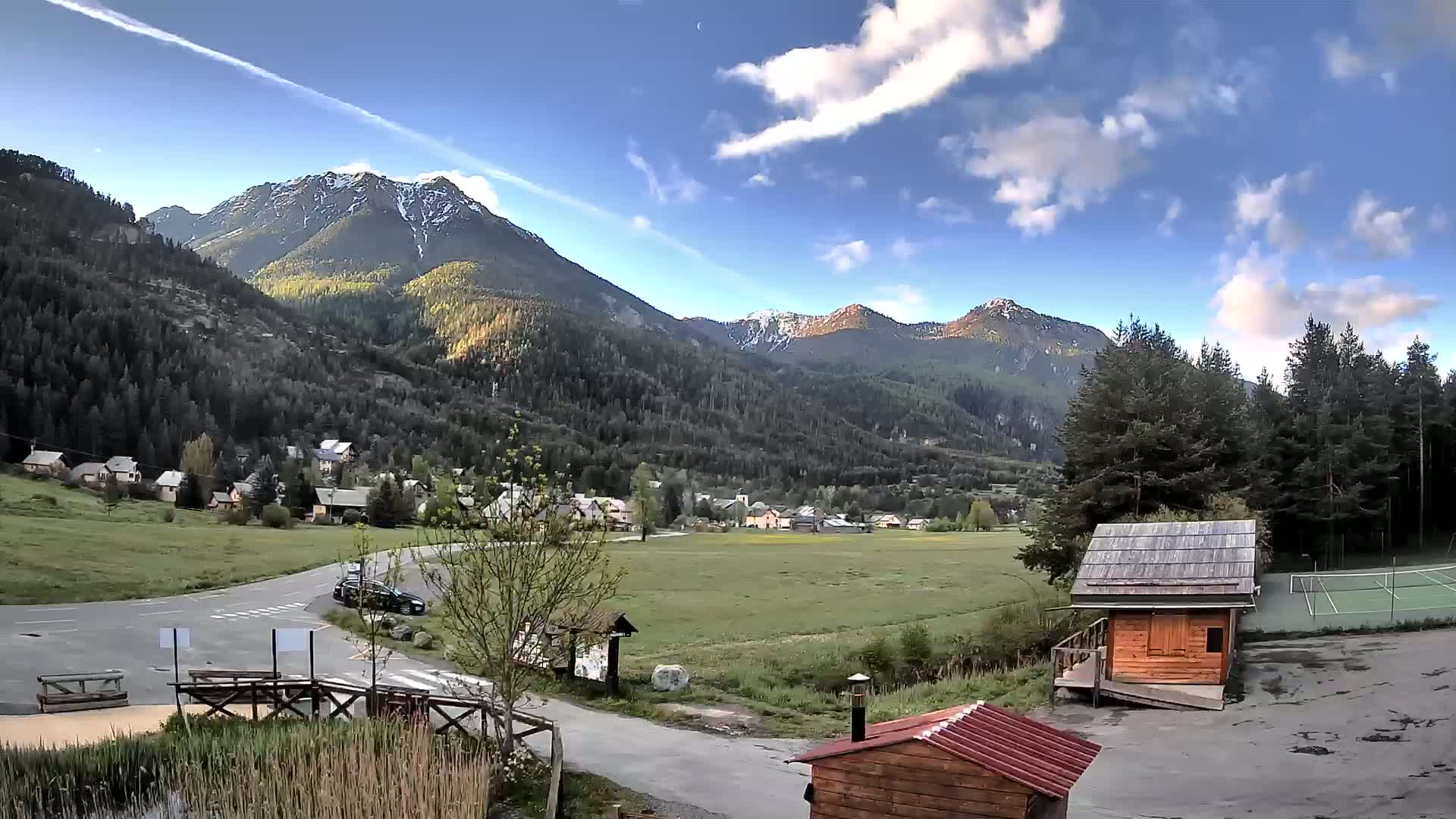 A small village nestled in a valley between snow-capped mountains under a partly cloudy sky.