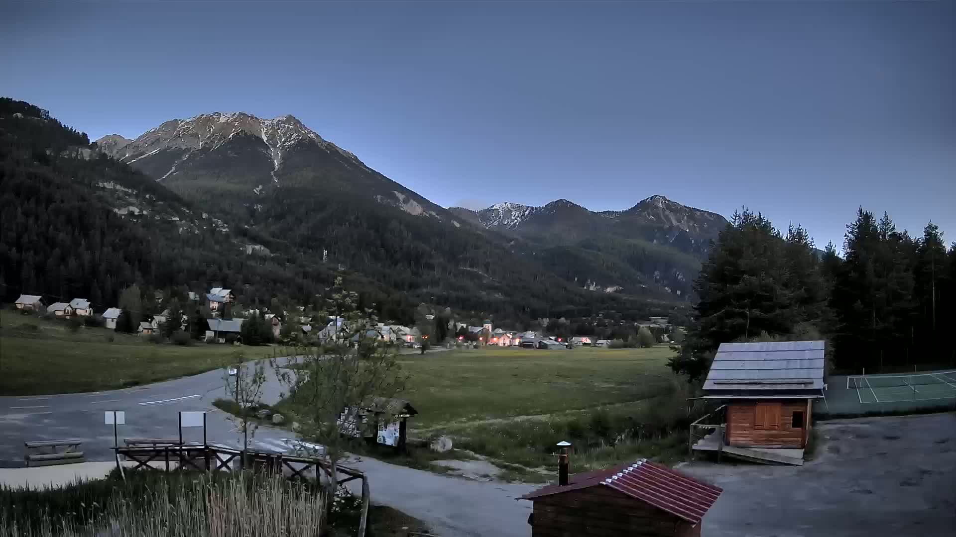 A small village nestled in a valley between snow-capped mountains under a clear, twilight sky.