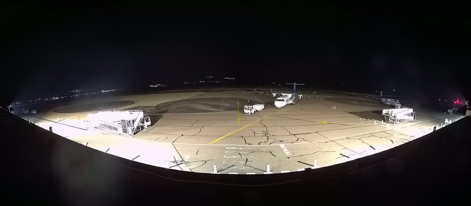 A plane is parked at night on an airport tarmac with ground support equipment and jet bridges, under a dark sky.