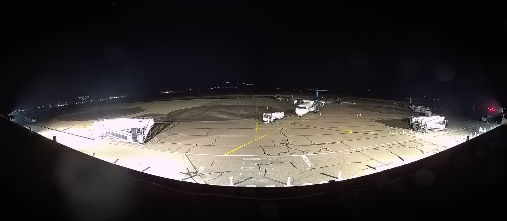 A plane is parked on a tarmac at night, with ground support equipment nearby, under clear skies.