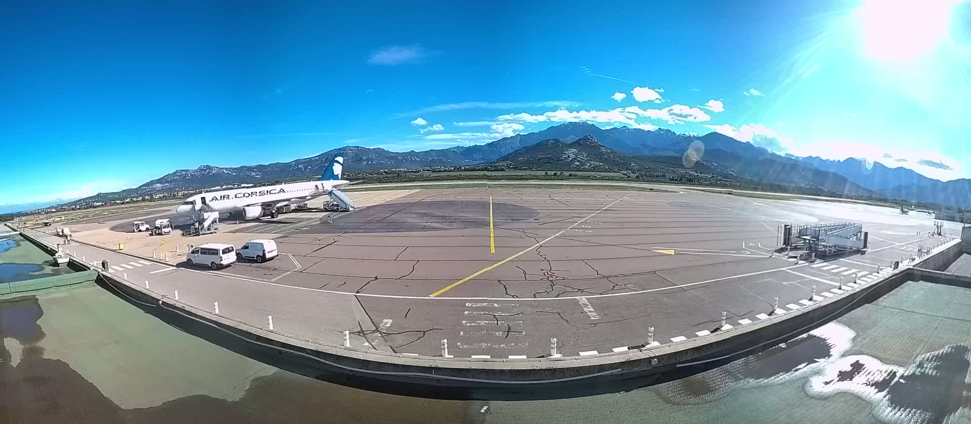 A passenger airplane is parked at an airport tarmac on a sunny day with mountains in the background.