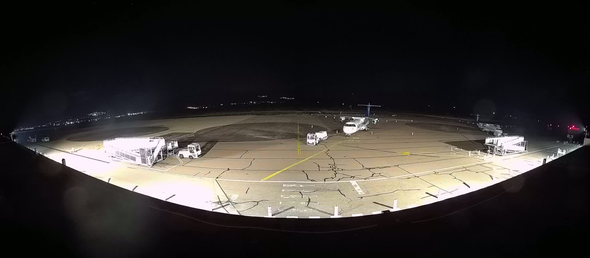 At night, an airplane is parked on a tarmac illuminated by ground lights, with ground support equipment nearby.