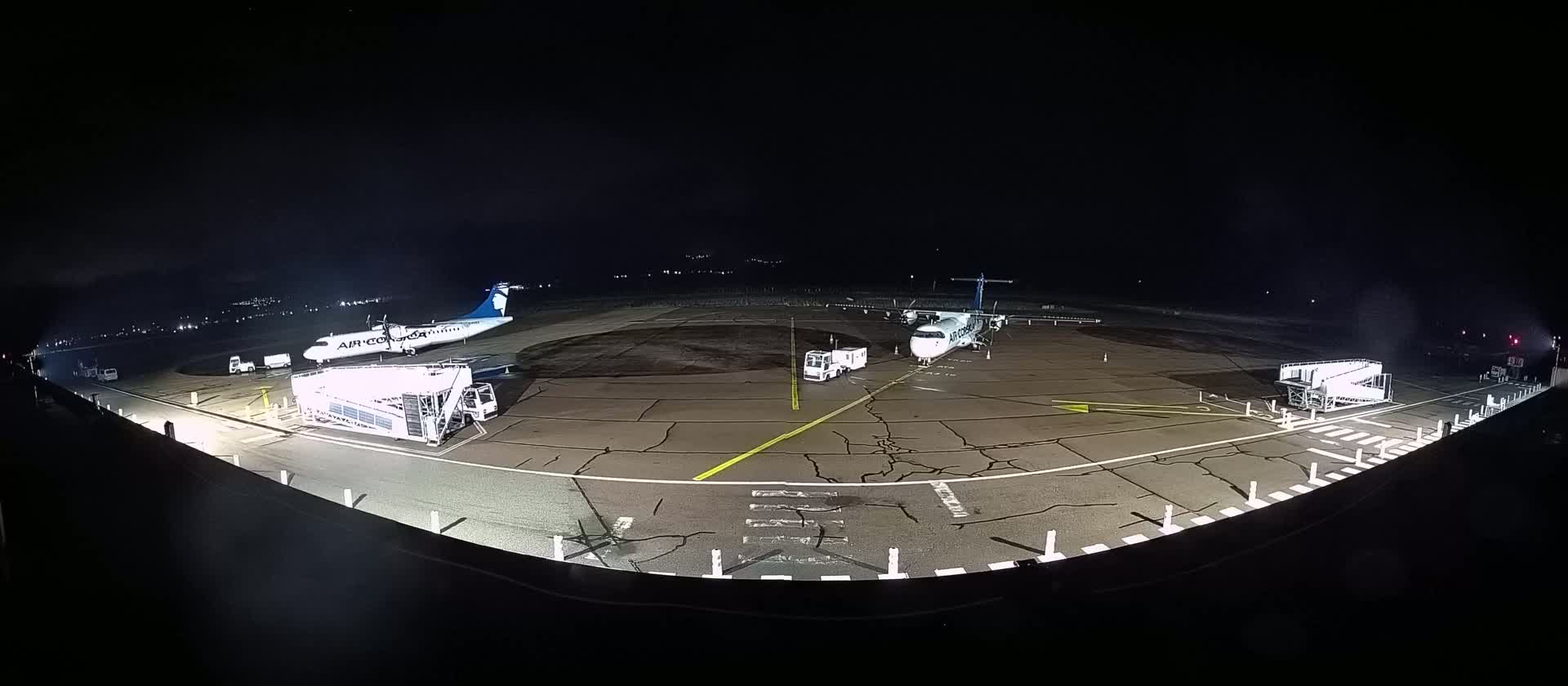 Two airplanes are parked at night on a tarmac next to passenger boarding bridges and support vehicles.