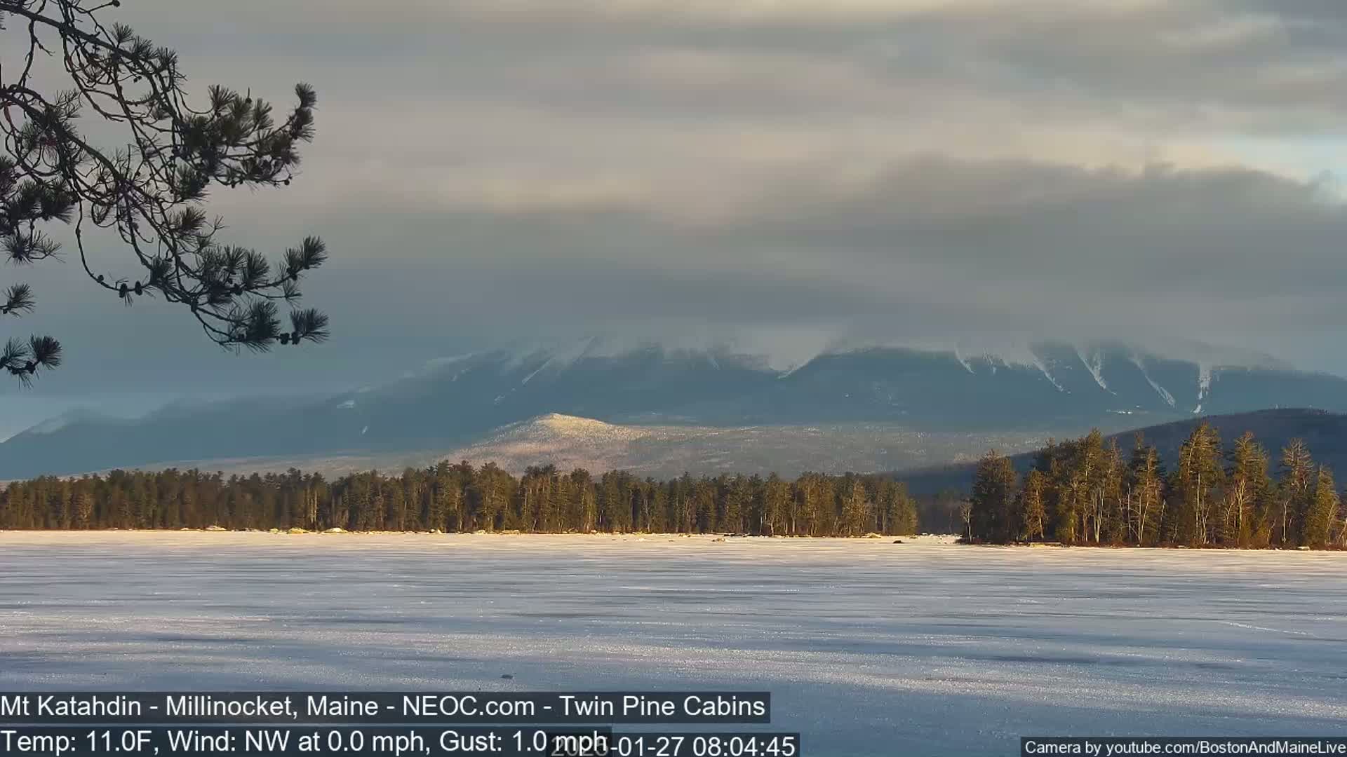 A frozen lake stretches before snow-dusted mountains under a mostly cloudy sky.