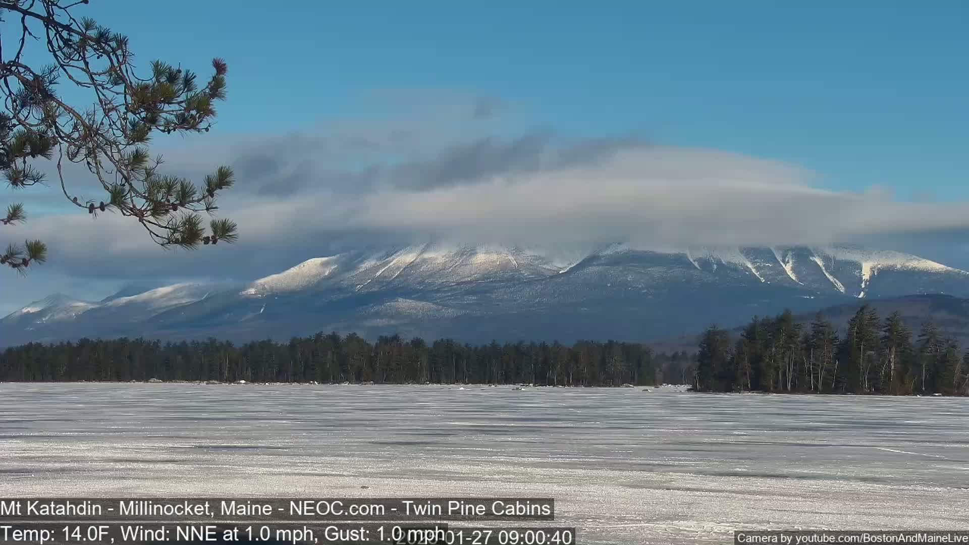 A snow-capped mountain range is seen in the distance across a frozen lake under a partly cloudy sky.