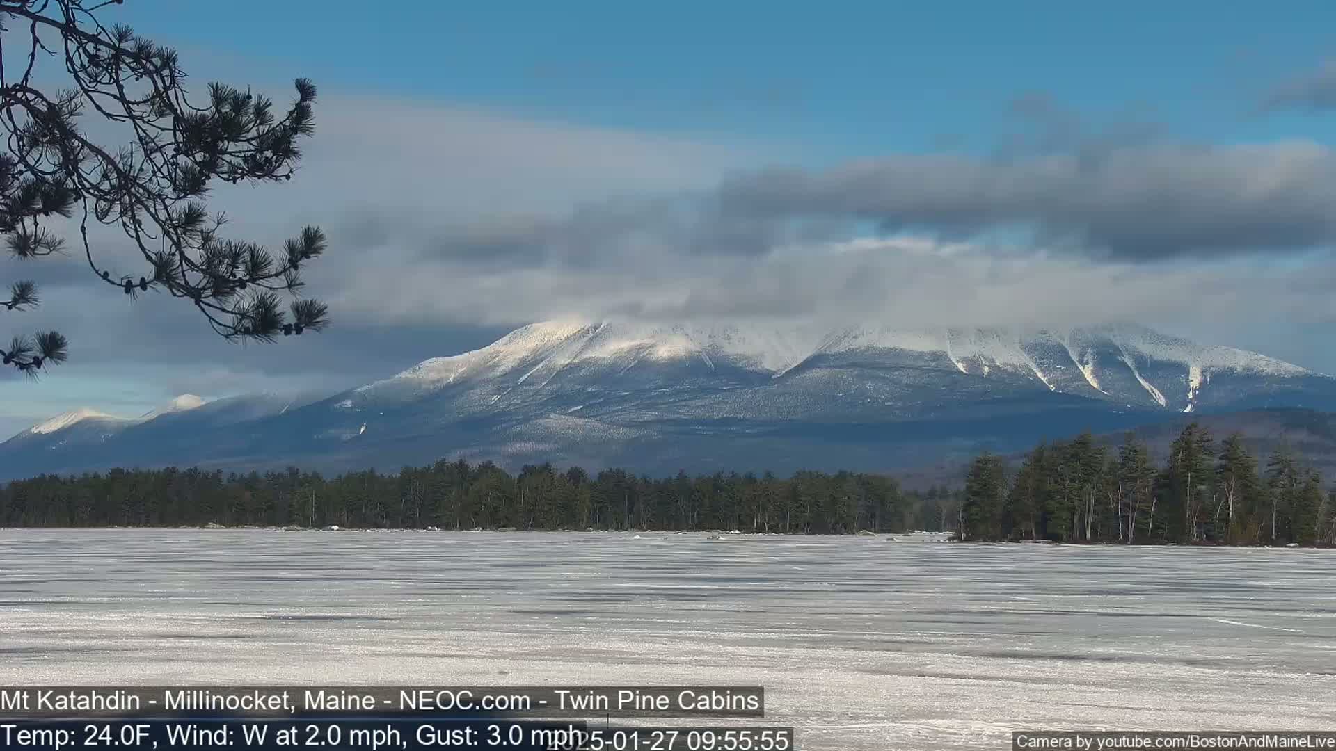 A snow-capped mountain range is visible in the distance behind a frozen lake under a partly cloudy sky.