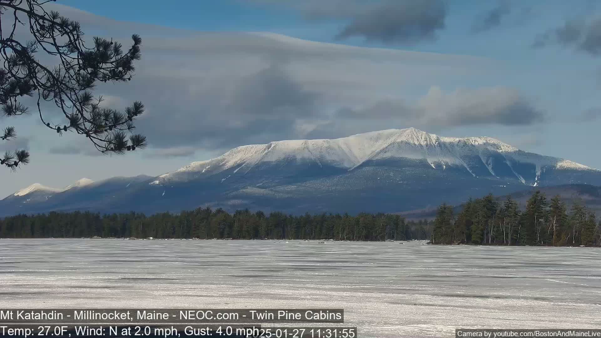 A snow-covered mountain range is visible in the distance beyond a frozen lake under a mostly cloudy sky.