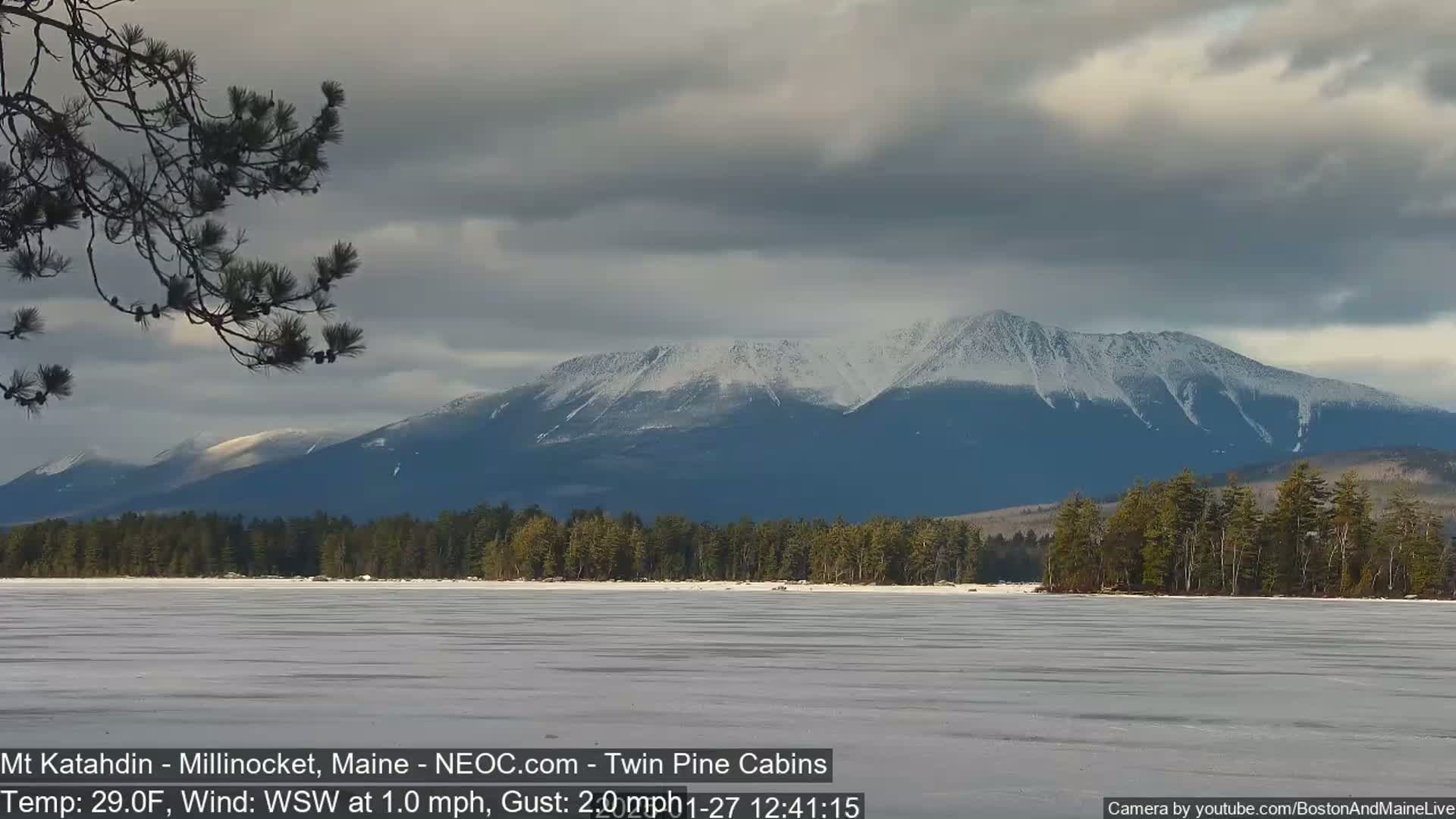 A snow-covered mountain range is visible in the distance behind a frozen lake, under a mostly cloudy sky.
