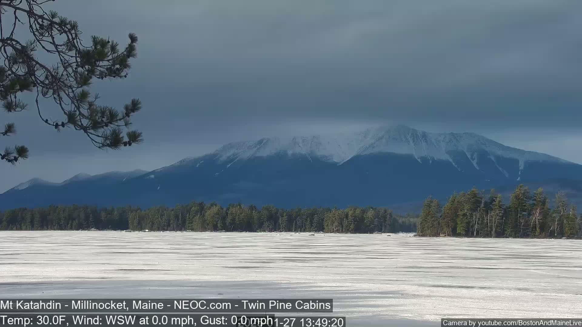 A snow-capped mountain range is seen in the distance across a frozen lake under an overcast sky.