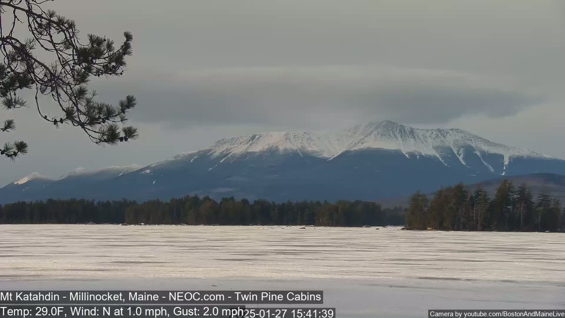 A snow-covered mountain range is visible in the distance across a frozen lake under an overcast sky.