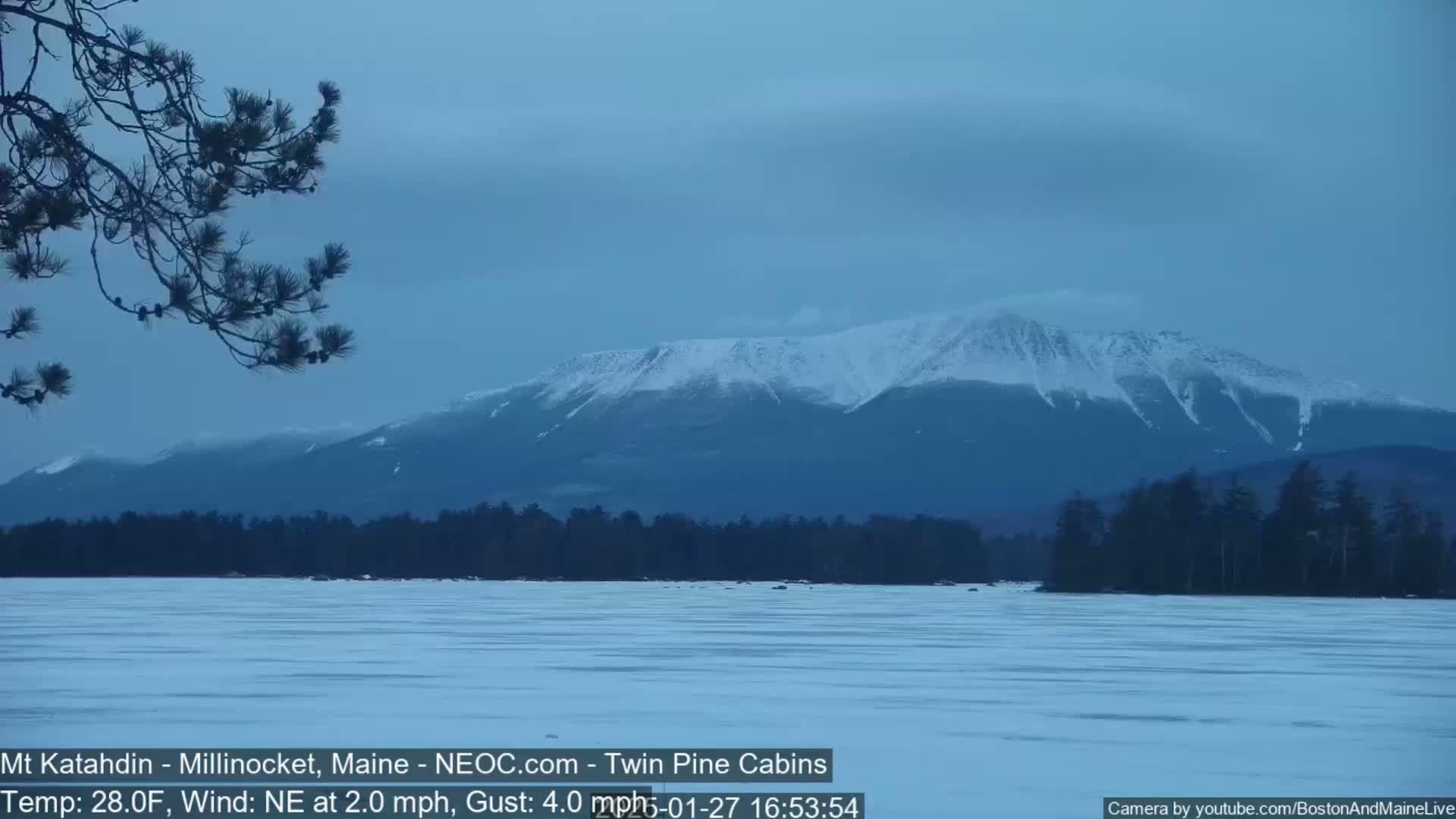 A snow-covered mountain range is visible in the distance across a frozen lake under a twilight sky.