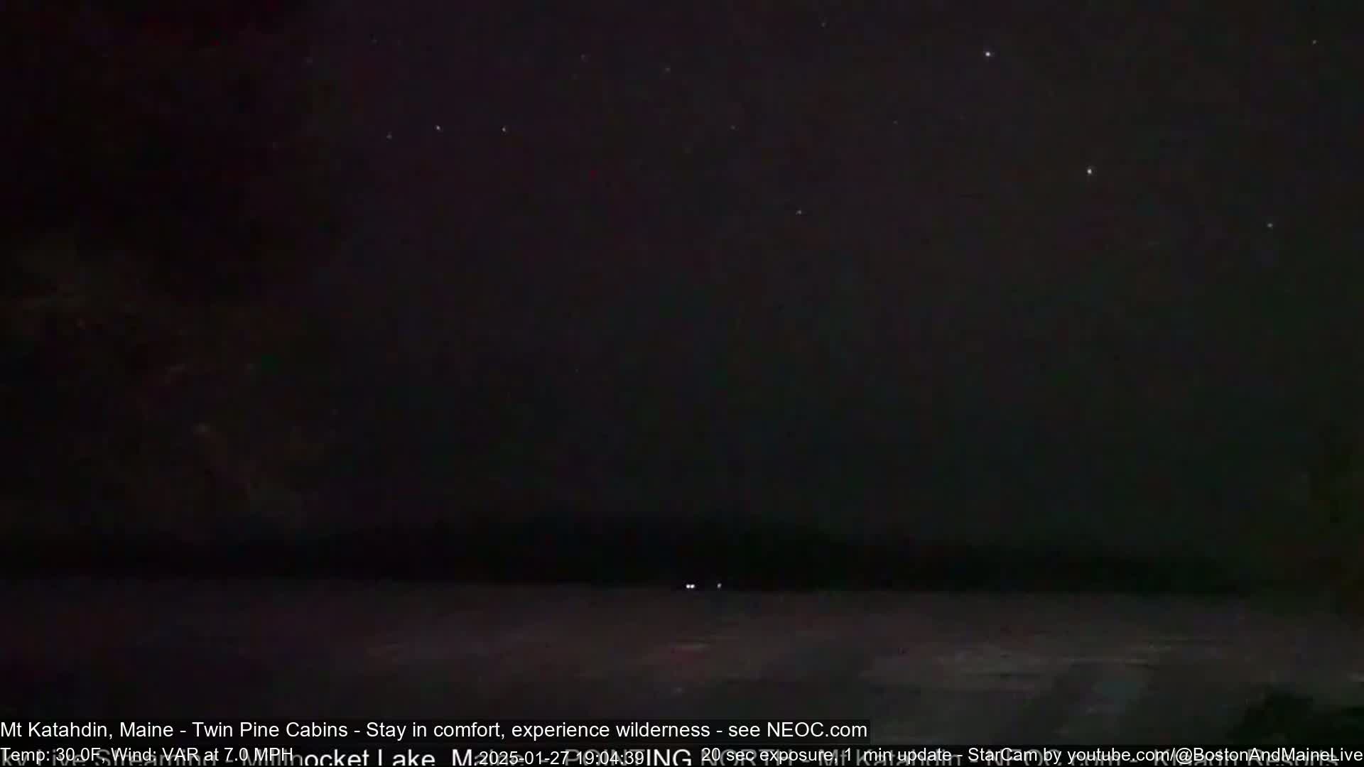 A dark, nighttime scene shows a mostly clear sky with stars visible above a dark, flat expanse of land or water.