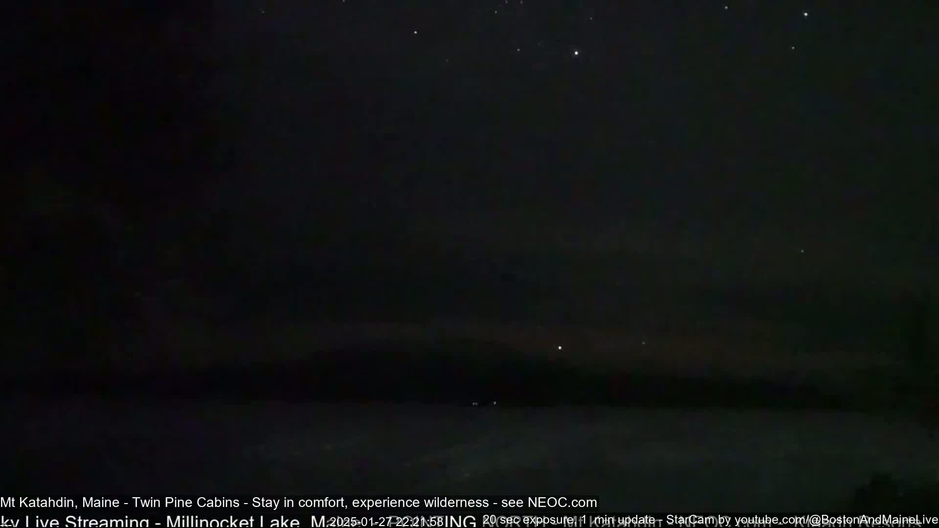A nighttime long exposure shot shows a dark, starlit sky over a dark, indistinct landscape.
