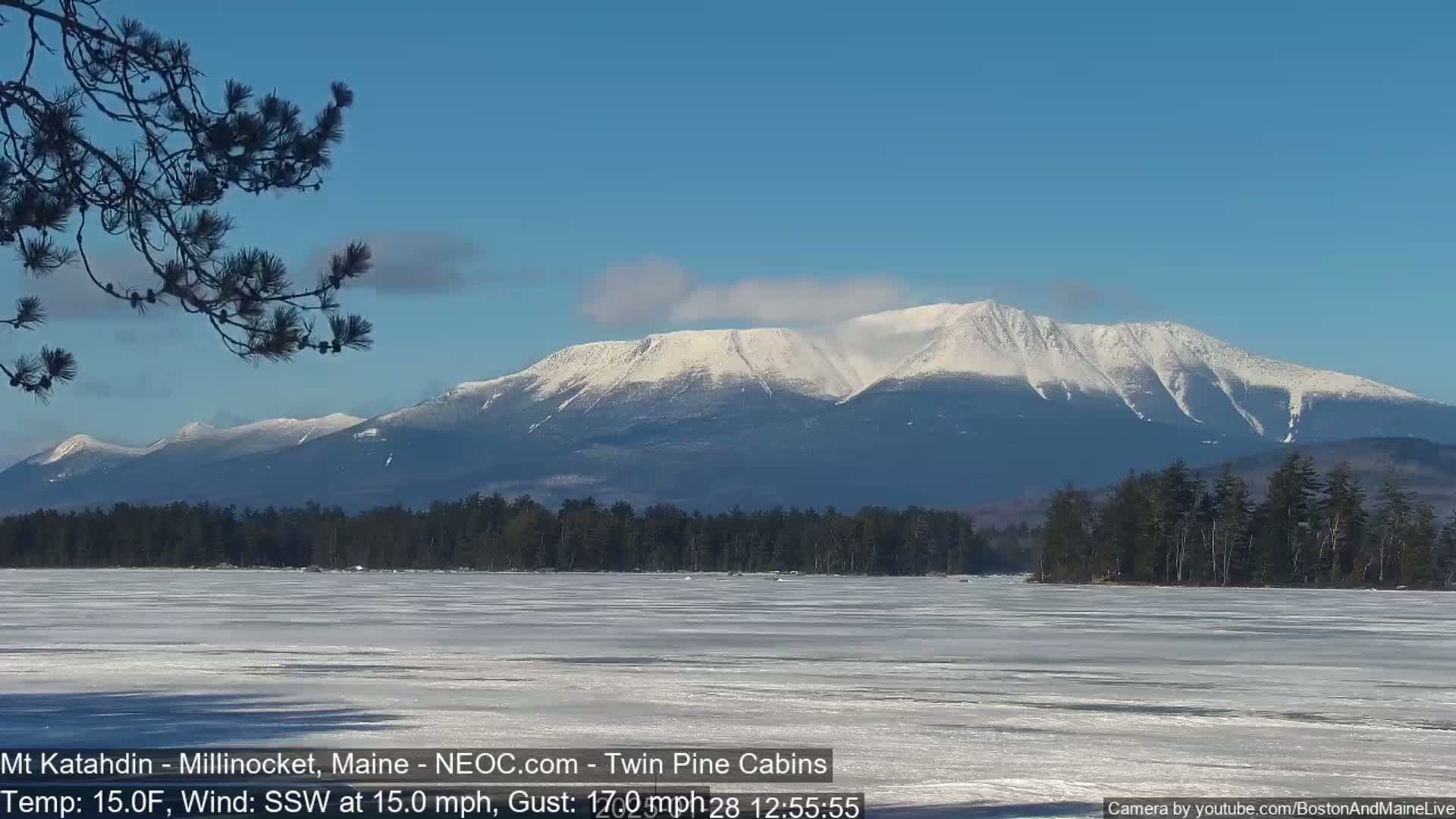 A snow-covered mountain range is seen in the distance across a frozen lake under a clear blue sky.