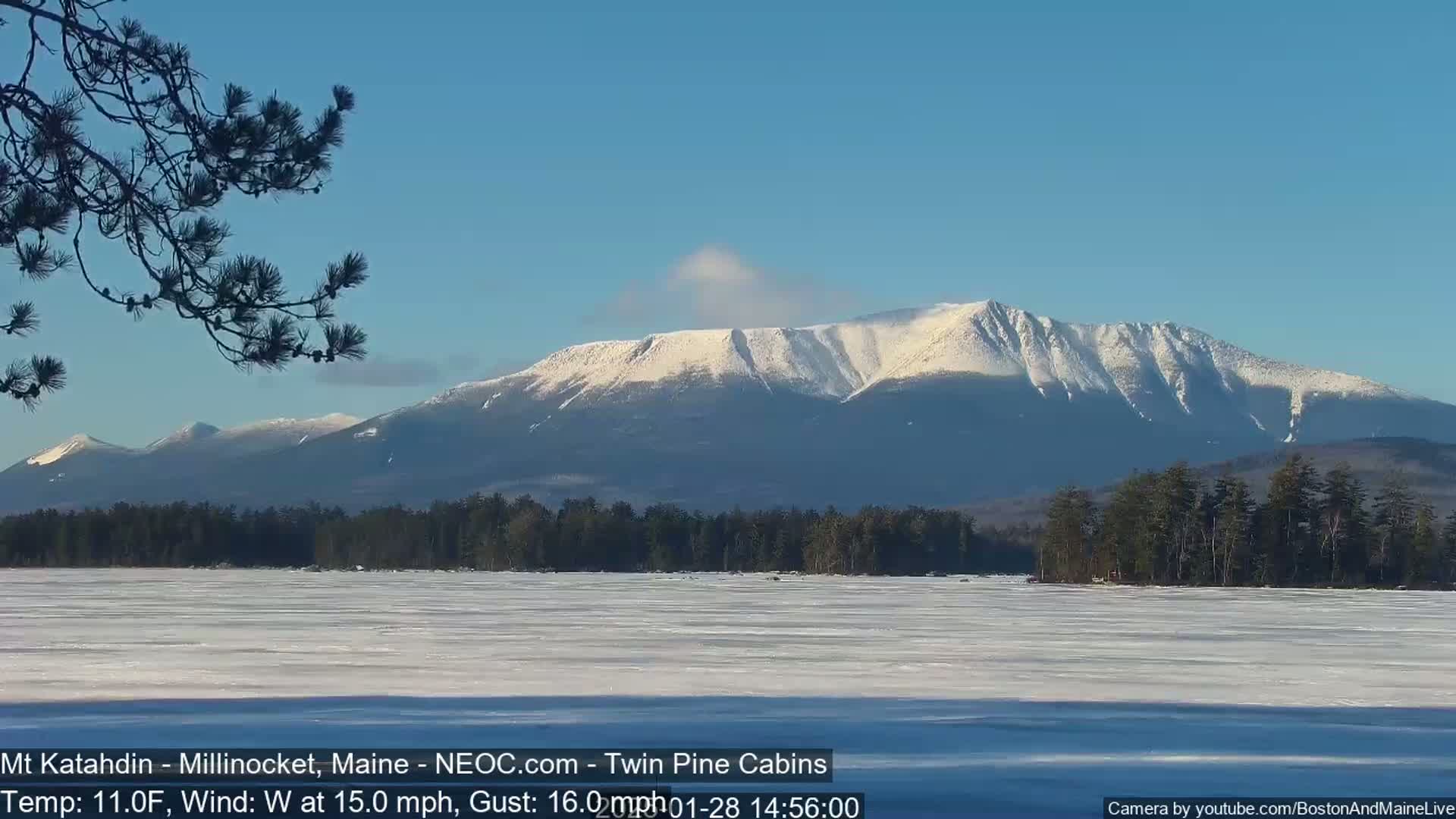 A snow-covered mountain range is visible across a frozen lake under a clear blue sky.
