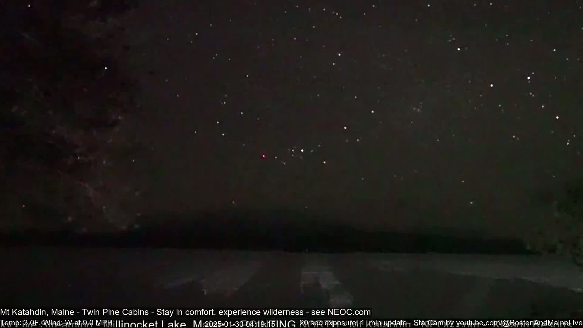 A nighttime long exposure shows a dark sky filled with stars over a dark, flat landscape.