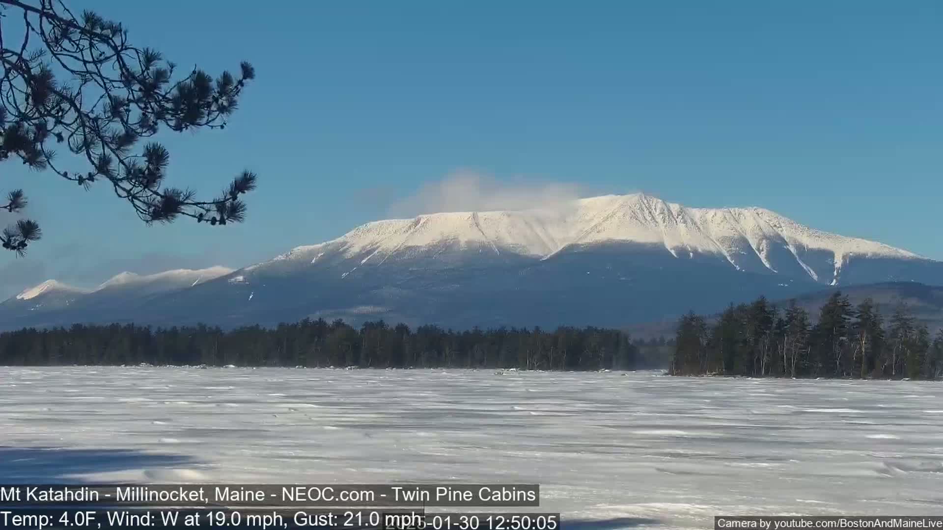A snow-covered mountain range is visible in the distance across a frozen lake, under a clear blue sky with a light wind.