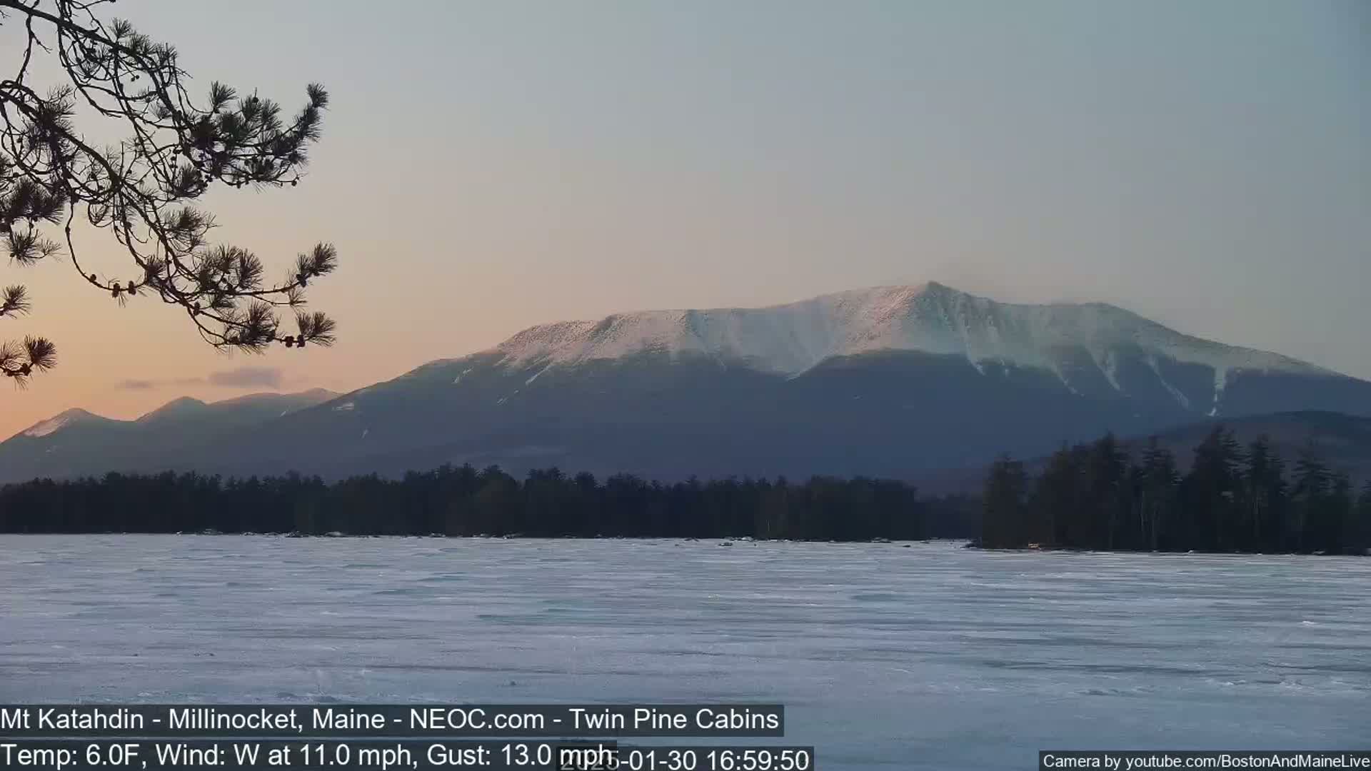 A snow-capped mountain range is visible in the distance across a frozen lake under a twilight sky.