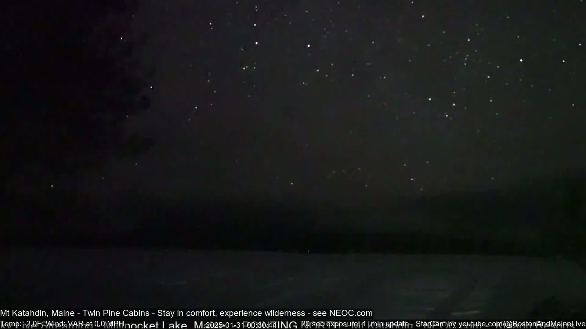 A dark, star-filled night sky is seen over a still body of water.