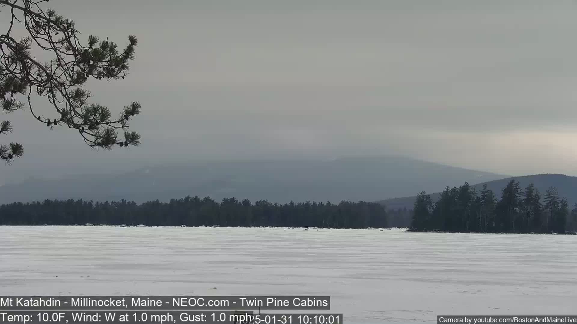 A snow-covered frozen lake extends to a distant, hazy mountain range under a gray sky.