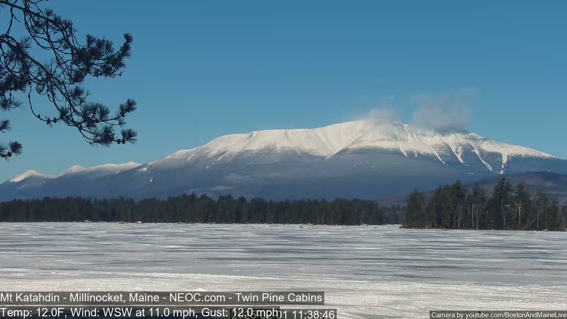 A snow-covered mountain range is visible in the distance across a frozen lake under a clear blue sky.