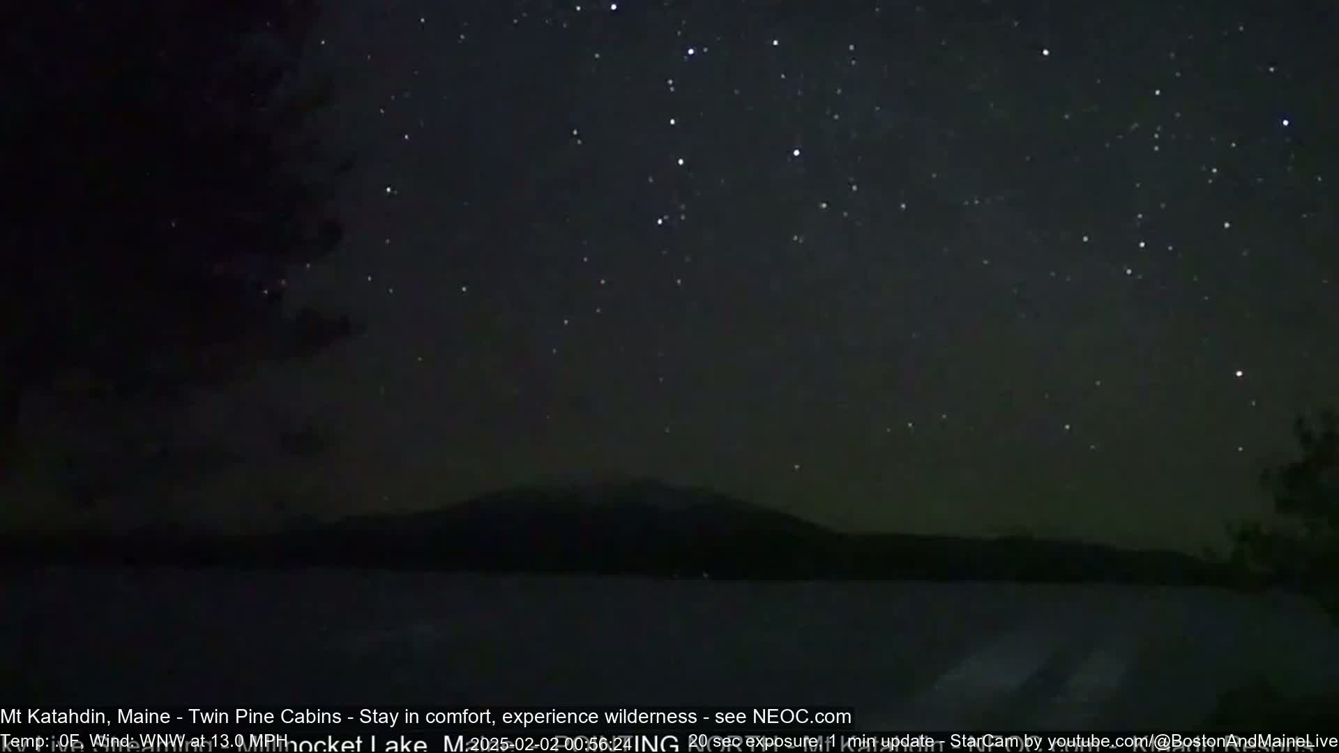 A dark, star-filled night sky is visible above a calm body of water with a mountain silhouetted on the horizon.
