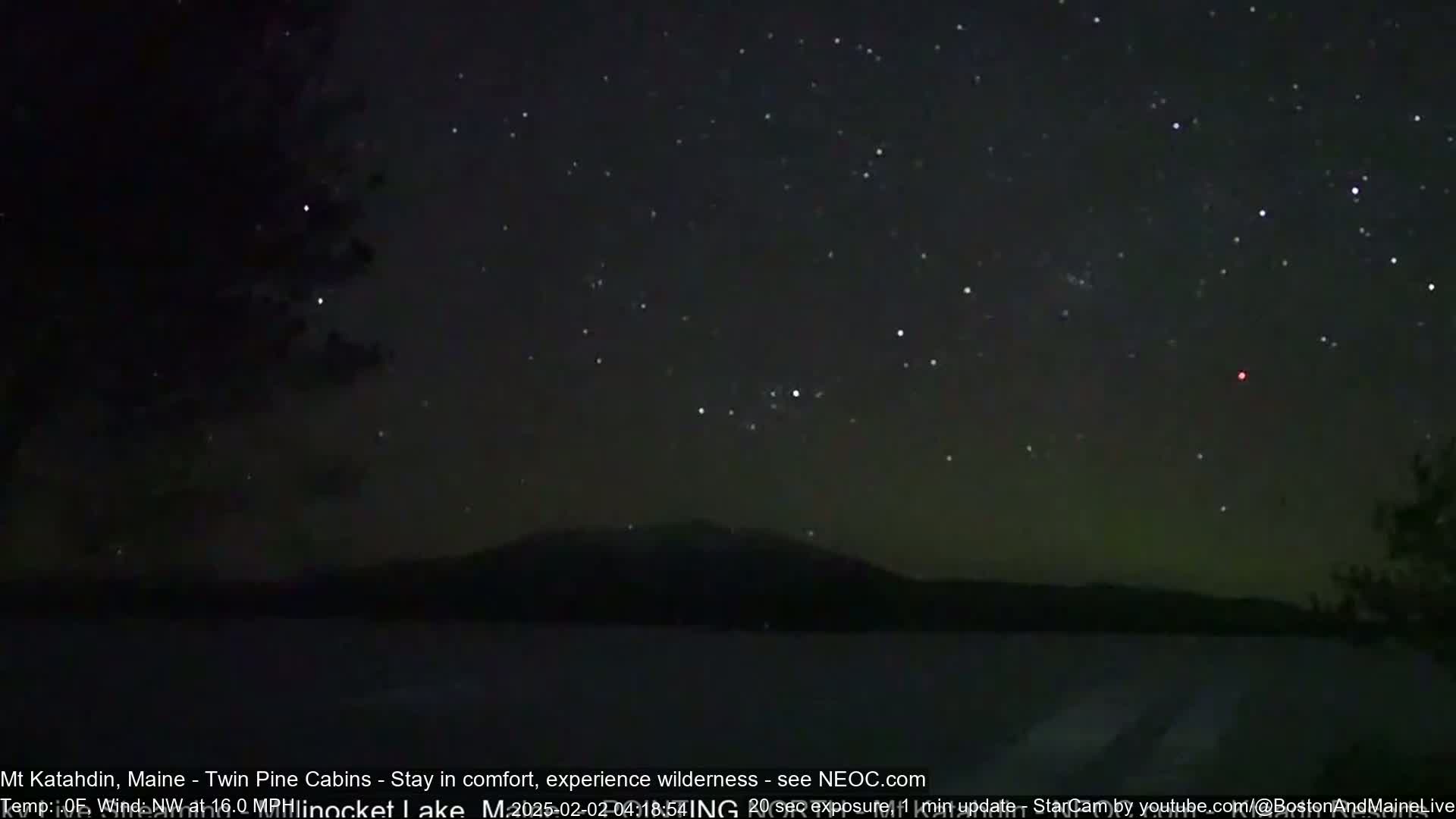 A dark, star-filled night sky over a silhouetted mountain range and a calm body of water.