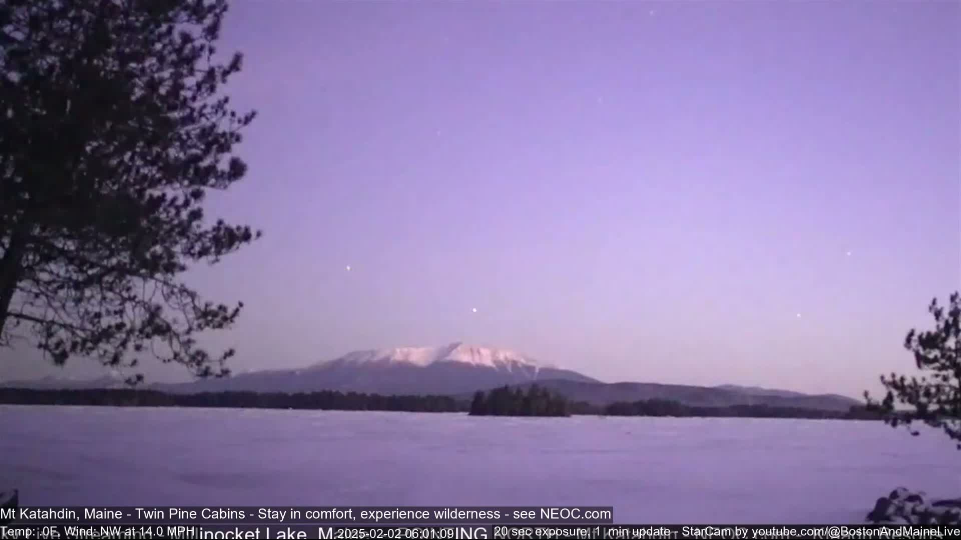 A snow-covered lake and a snow-capped mountain are visible under a pale purple twilight sky.