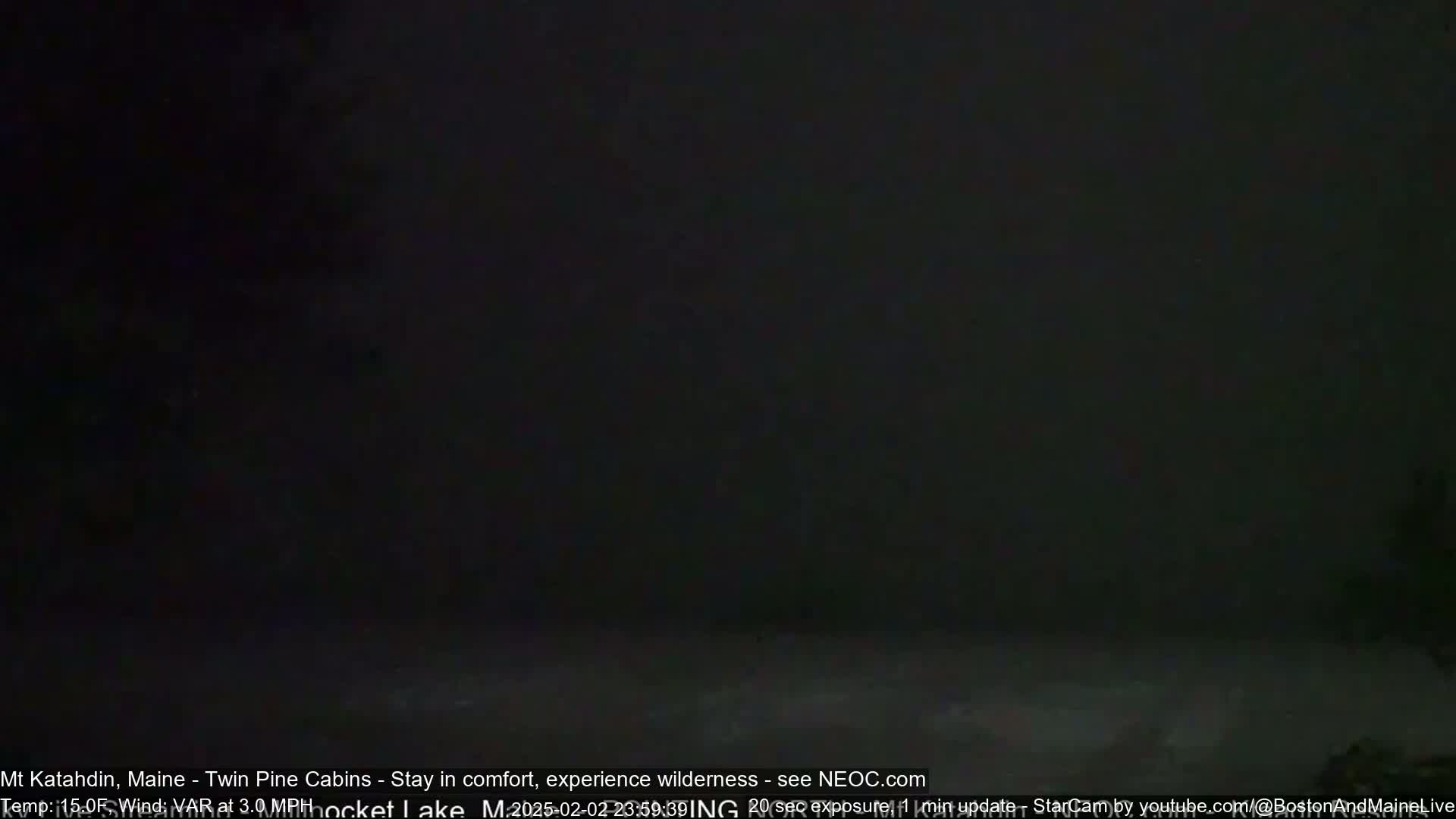A dark, nighttime scene shows a mostly obscured view of an area with a light dusting of snow on the ground under a dark sky.