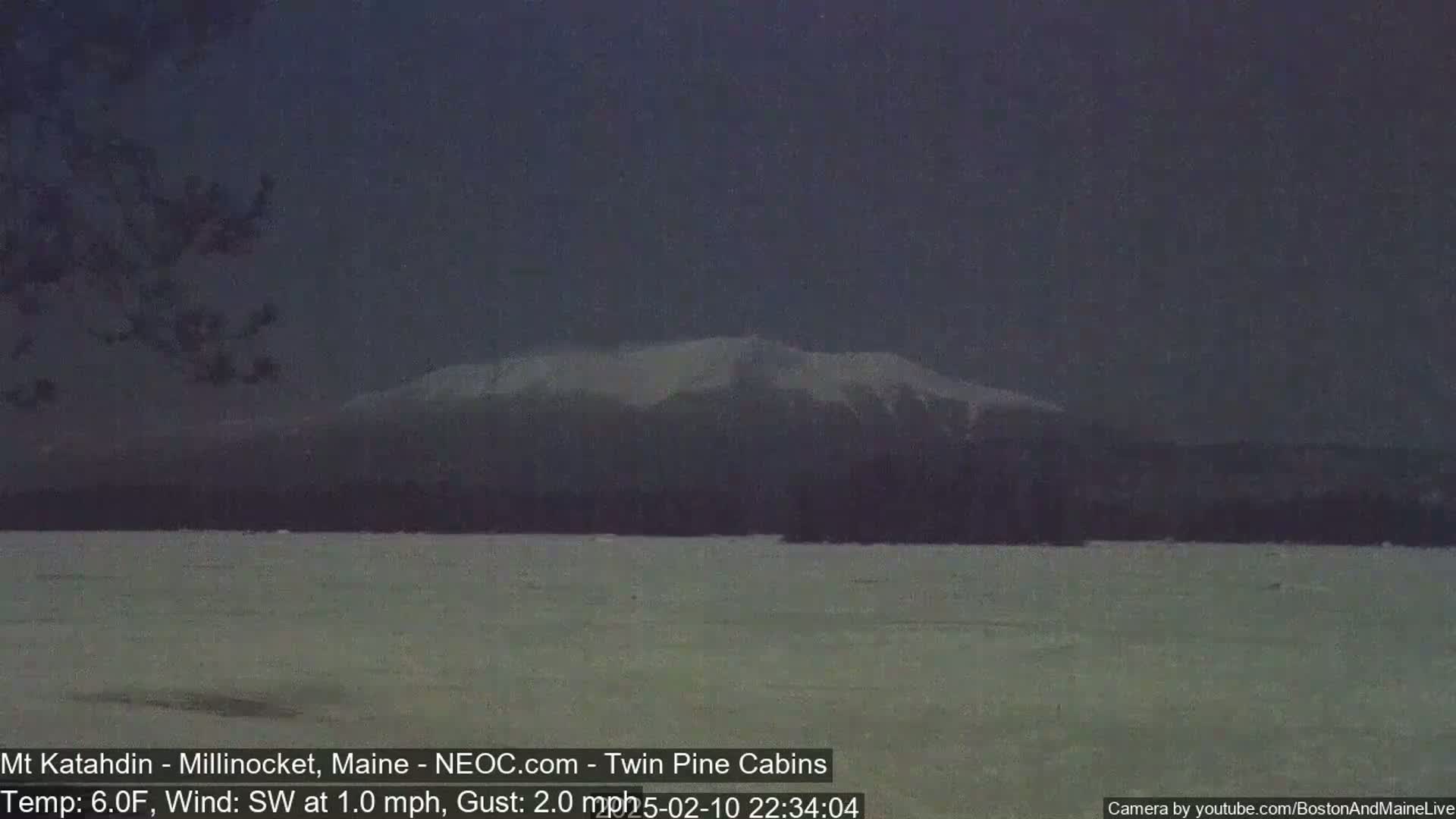A snow-capped mountain is visible in the distance across a flat, snow-covered expanse under a dark, overcast sky.