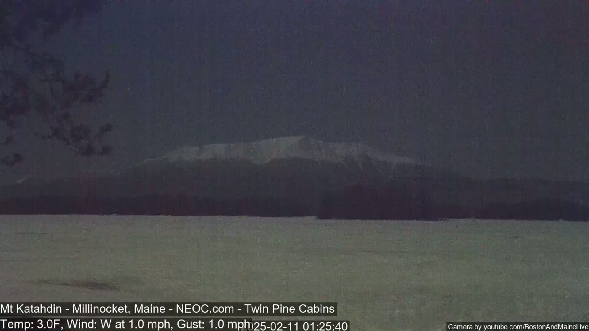A snow-covered mountain range is visible in the distance under a dark, nighttime sky, with a flat, snow-covered plain in the foreground.