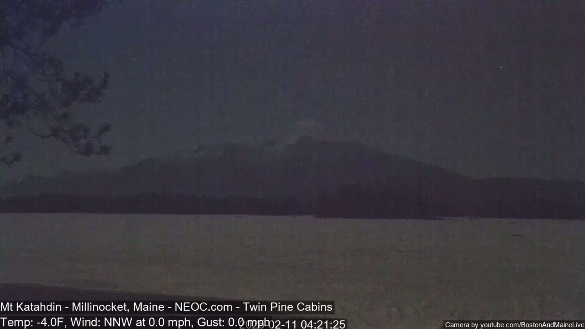 A dark, calm lake stretches out to a distant, silhouetted mountain range under a dusky sky.