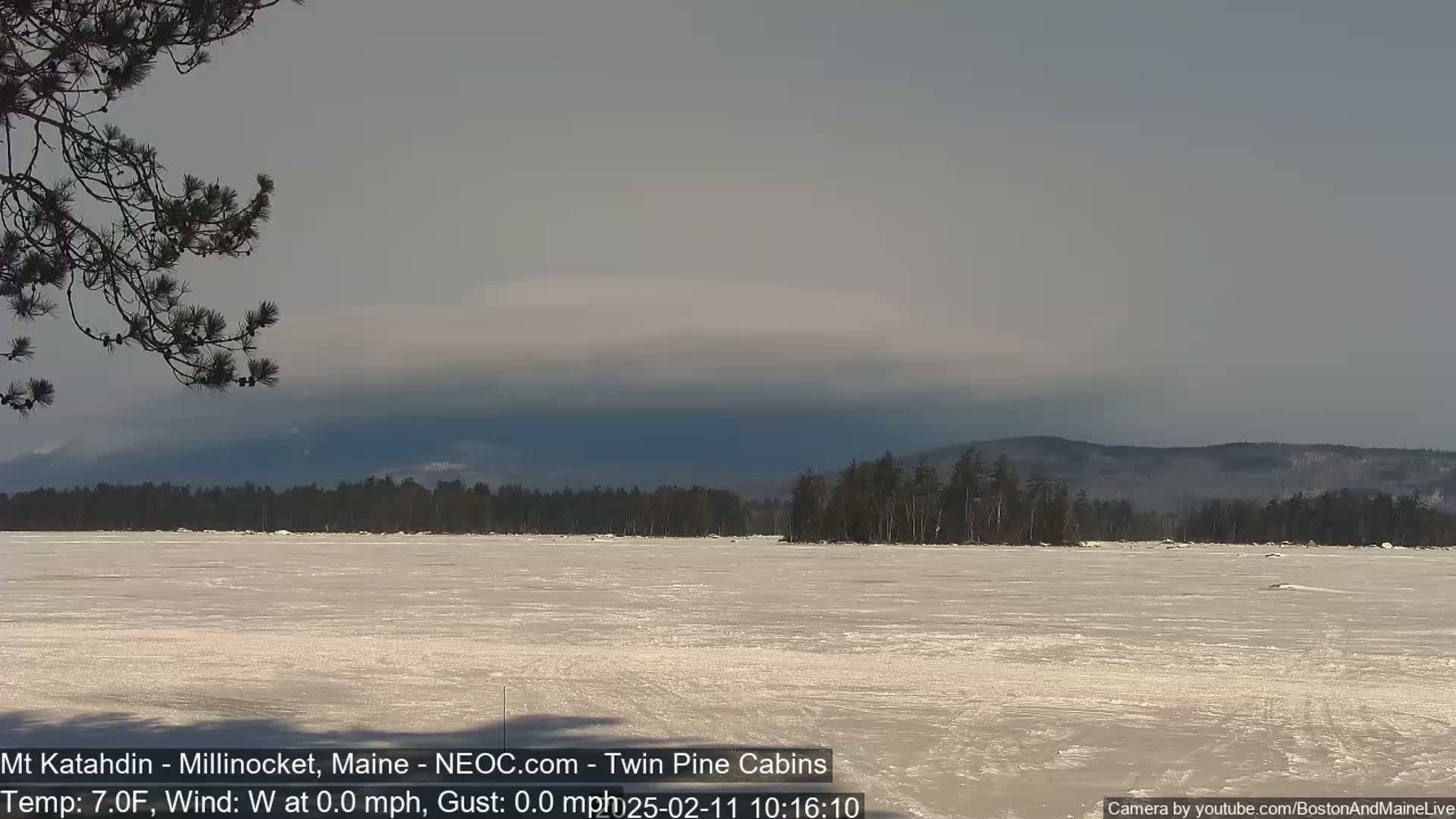 A frozen lake stretches to a distant mountain range under a mostly cloudy sky.