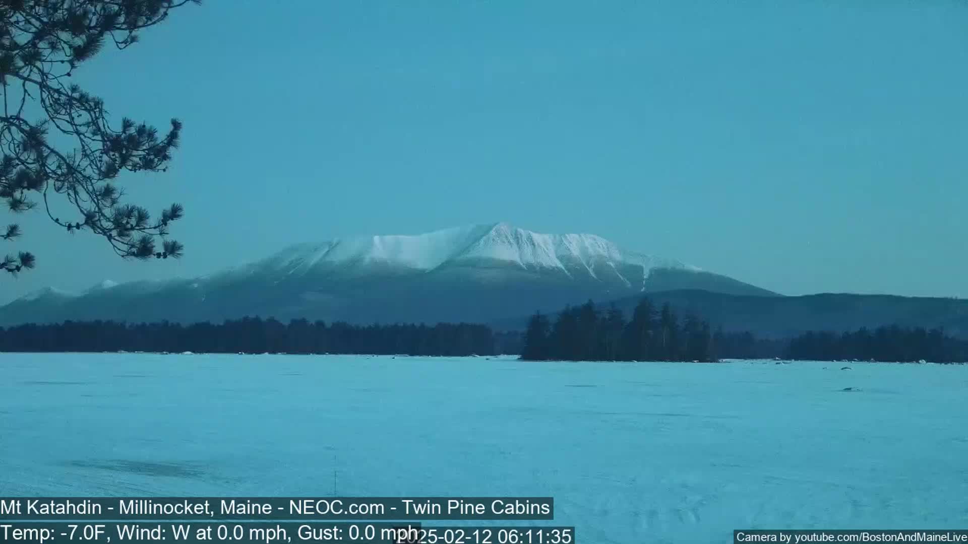 A snow-covered mountain range is visible in the distance across a frozen, calm lake under a clear, pale blue sky.