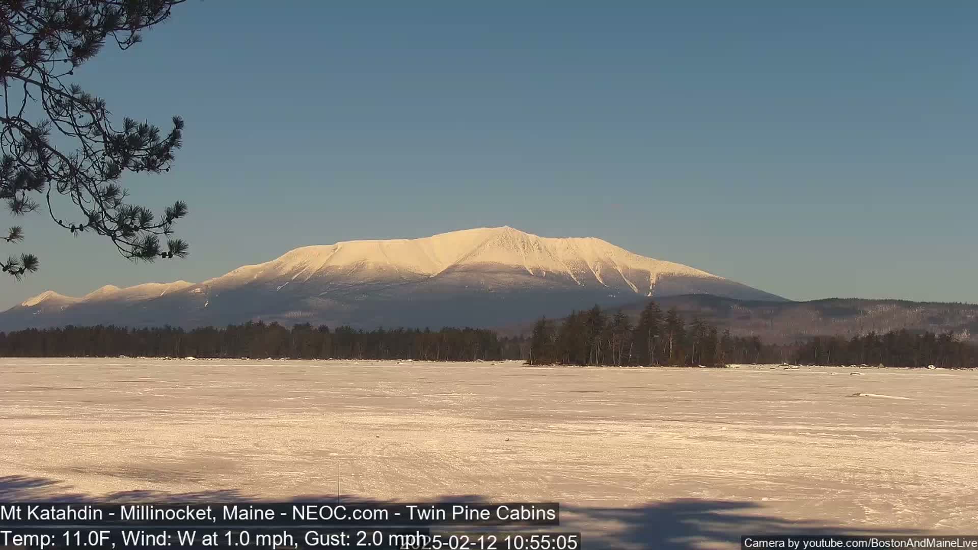 A snow-covered mountain range is visible in the distance across a frozen lake under a clear, bright sky.