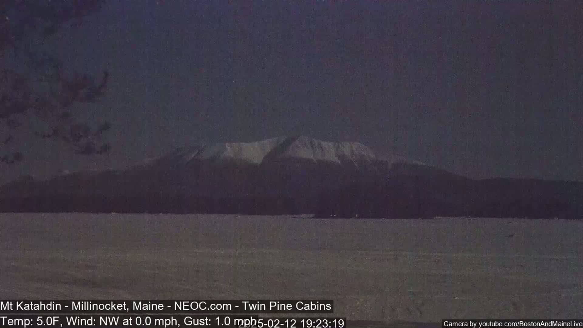 A snow-covered mountain range is visible at dusk over a dark, frozen body of water.