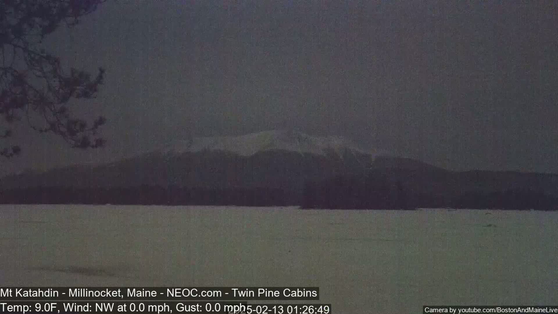A snow-covered landscape shows a distant mountain range under a dark, overcast sky.
