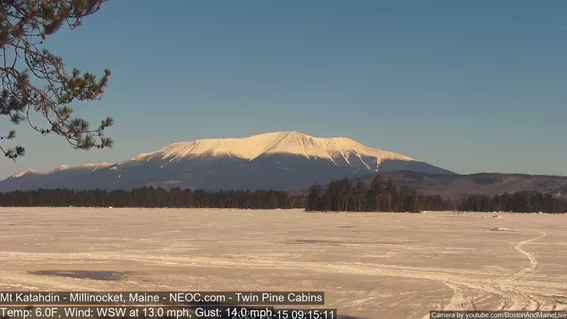 A snow-covered mountain is seen in the distance across a frozen lake under a clear, blue sky.