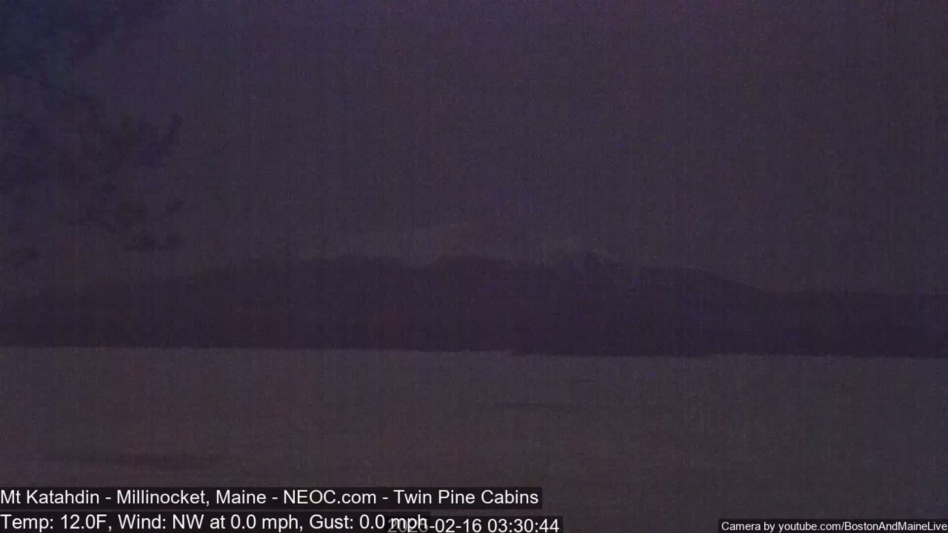 A dark, still body of water is shown with a dimly lit mountain range in the background under a dark sky.