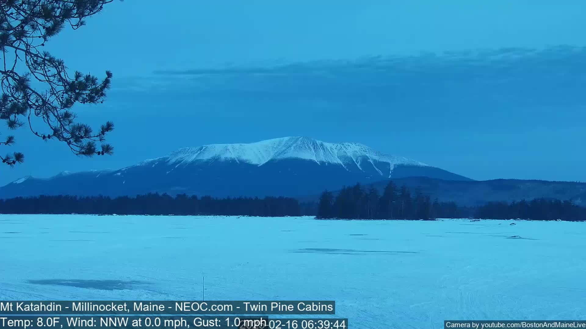 A snow-covered mountain range is visible in the distance across a frozen lake under a clear, twilight sky.